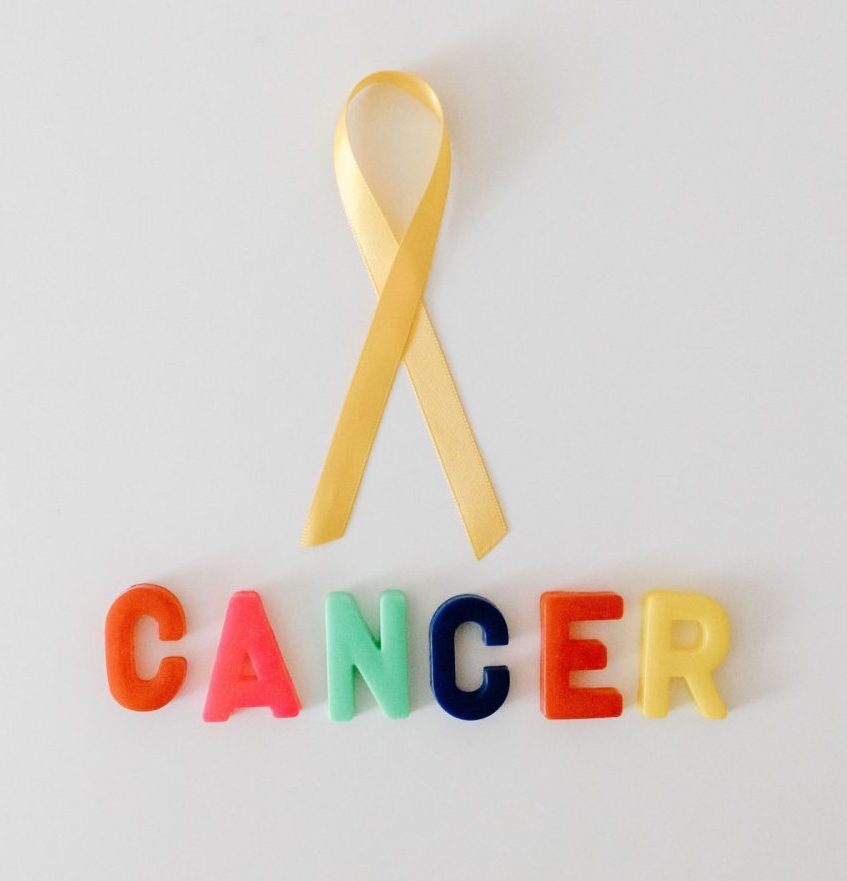Yellow cancer awareness ribbon with colorful letters spelling 'cancer' on white background.